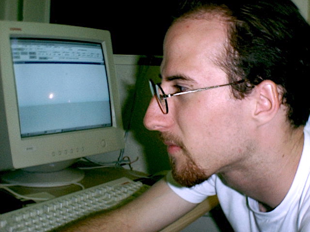 Man with goatee facial hair and glasses looking at a computer in 1999.